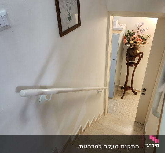 מעקה אחיזה ממתכת לבנה המותקן על קיר לצד מדרגות פנים